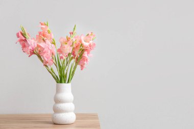 Vazo dolusu güzel gladiolus çiçekleriyle ahşap masada beyaz arka planda.