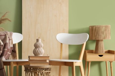 Ekose, vazo ve kitaplarla dolu sandalyeler yeşil duvarın yanında duruyor.