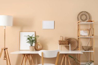 Raflama ünitesi, lamba ve bej duvarın yanındaki ev bitkileriyle şık bir iş yeri.