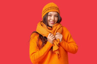 Kırmızı arka planda örgü şapkalı ve atkılı güzel bir Asyalı kadın.