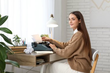 Masada oturan daktilo ve not defteriyle güzel, mutlu kadın yazar.