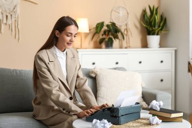 Güzel, mutlu, daktilo, kitap ve buruşuk kağıtlı bir kadın yazar evdeki kanepede oturuyor.