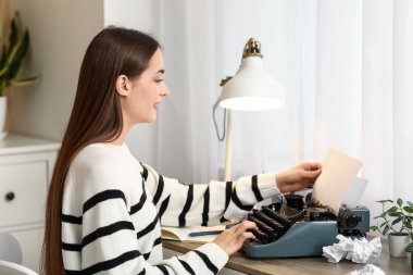 Masada oturan daktilo ve not defteriyle güzel, mutlu kadın yazar.