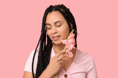 Pembe arka planda gladyatör çiçeğiyle güzel bir Afro-Amerikalı kadın.
