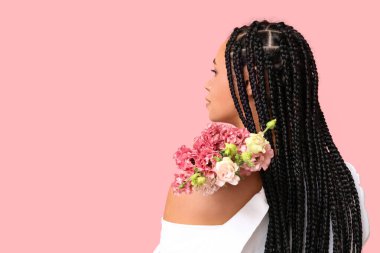 Pembe arka planda Eustoma çiçekleri olan genç bir Afro-Amerikalı kadın.