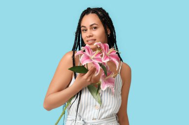 Mavi arka planda pembe zambak çiçekleri olan güzel bir Afro-Amerikalı kadın.