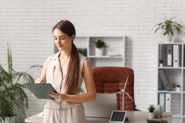 Ofisteki masasında pano ve rüzgar türbini modeli olan genç bayan mühendis.