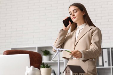 Ofiste rüzgar türbini modeliyle cep telefonuyla konuşan kadın mühendis.