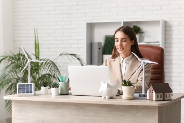 Ofisteki masada dizüstü bilgisayar ve rüzgar türbinleriyle çalışan kadın mühendis.