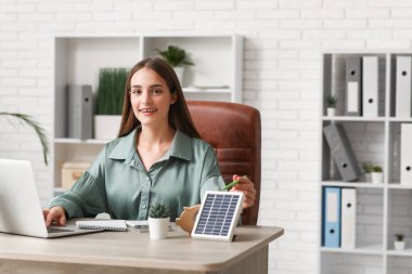 Ofiste çalışan dizüstü bilgisayarı ve taşınabilir güneş paneli olan kadın mühendis.
