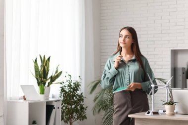 Ofisteki masasında dizüstü bilgisayarı ve rüzgar türbini modelleriyle düşünceli kadın mühendis.