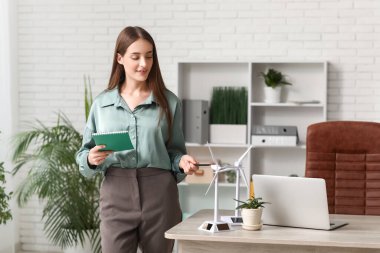 Ofisteki masasında dizüstü bilgisayarı ve rüzgar türbini modelleri olan kadın mühendis