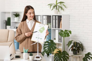 Ofisteki masasında pano ve rüzgar türbini modeli olan kadın mühendis.