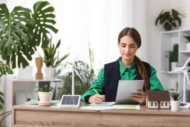 Ofisteki masada tablet bilgisayar ve rüzgar türbini modelleriyle çalışan kadın mühendis.