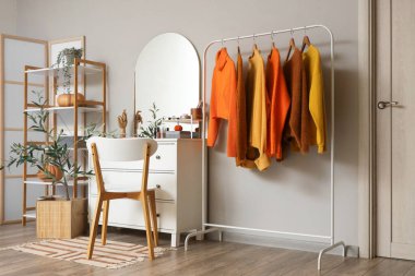 Aynalı şık giyinme odası, çekmeceler ve askıda asılı sonbahar giysileri.