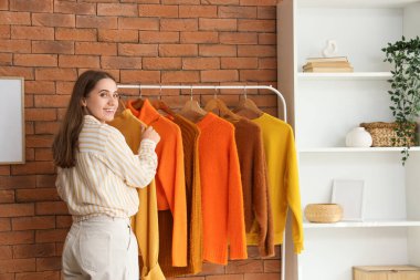 Güz kıyafetlerini soyunma odasından alan güzel genç bir kadın.