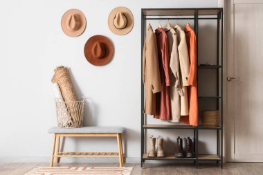 Gri banklı, şapkalı ve sonbahar kıyafetleri askıda asılı şık bir soyunma odası.