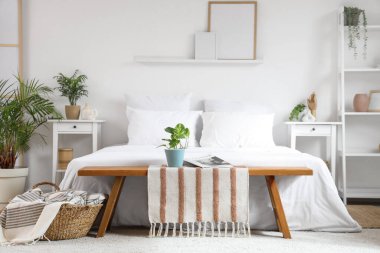 Yatak odasının içinde bank, yatak, komodin ve çiçek var.