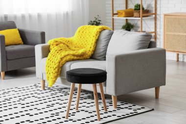 Modern oturma odası, şık gri kanepe, tabure ve sarı ekose örgü.