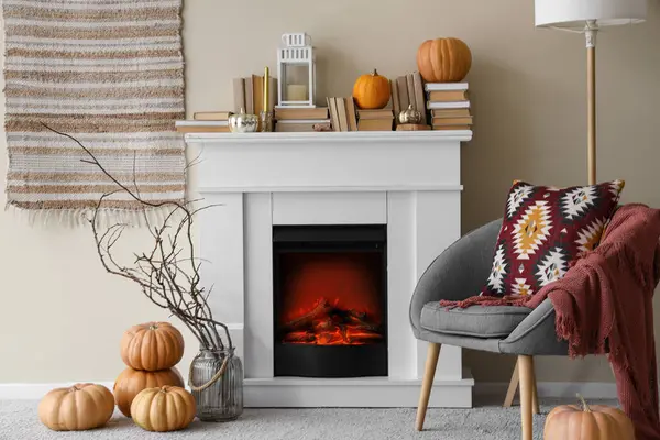 Beyaz şömineli, yumuşak koltuklu, balkabaklı ve kitaplı aydınlık oturma odasının içi.