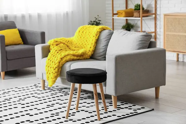 Modern oturma odası, şık gri kanepe, tabure ve sarı ekose örgü.