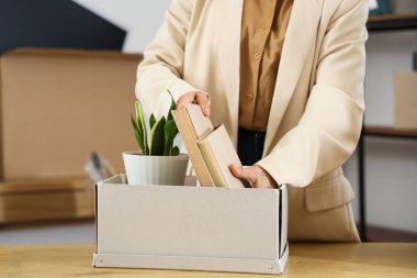 Olgun bir iş kadını taşınma gününde kitapları kutuya koyar, kapatır.