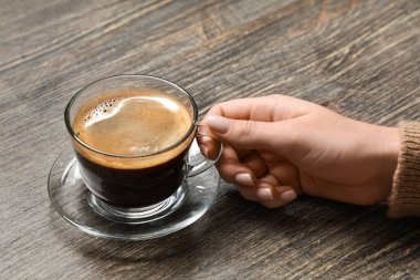 Ahşap arka planda bir fincan kahveyle kadın eli.