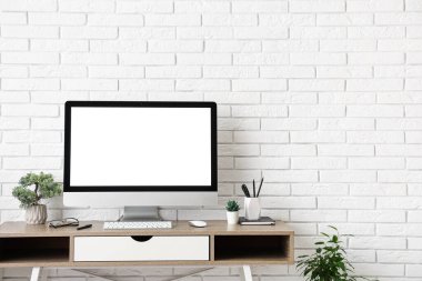 Işık ofisindeki beyaz tuğla duvarın yanında bilgisayar ve kırtasiye malzemesi olan şık bir iş yeri