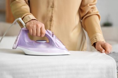 Evde çarşaf ütüleyen genç bir kadın.