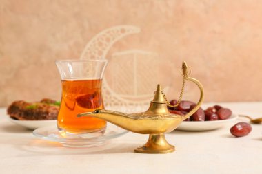 Aladdin lambası ve bej arka planda beyaz masada bir bardak çay. Ramazan kutlaması