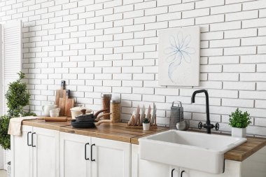 Lavabo, ev bitkileri ve çatal bıçaklar mutfaktaki beyaz tuğla duvarın yanında.