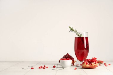 Biberiyeli bir bardak taze nar suyu ve beyaz fayans masasında bir kase tohum.