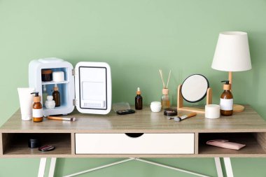 Küçük kozmetik buzdolabı, ayna ve lamba olan masa yeşil duvarın yanında. Yakın çekim.