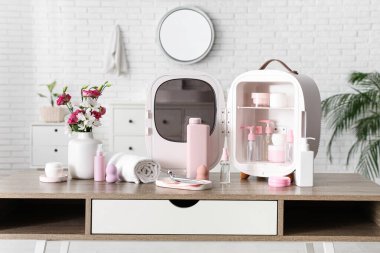 Beyaz duvarın yanındaki vazoda, içinde cilt ürünleri, havlu ve çiçekler olan açık kozmetik buzdolabı. Yakın çekim.