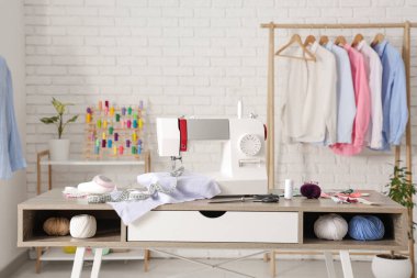 Terzinin dikiş makinesi, farklı malzemeler ve atölyedeki elbise rafı.