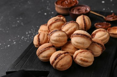 Siyah arka planda kaynamış yoğunlaştırılmış sütle ceviz şeklinde kurabiyeler kesme tahtası.