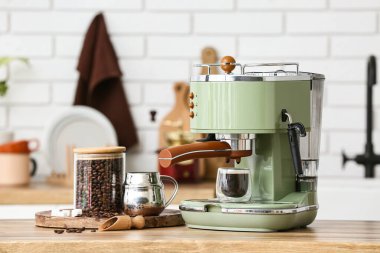 Mutfaktaki ahşap masada bir bardak sıcak espresso ve bir kavanoz fasulye ile modern kahve makinesi.