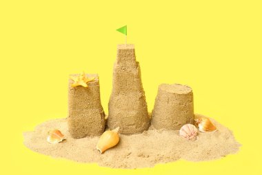 Güzel kumdan kale, sarı arka planda deniz kabukları.