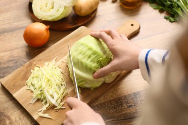 Mutfakta leziz borş çorbası için tahta tahtada lahana doğrayan genç bir kadın. Yakın çekim.