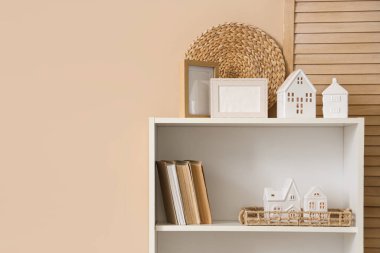 Resim çerçeveli raflar, kitaplar ve mum tutacaklı oda içinde bej duvarın yanındaki ev şeklinde, yakın plan.