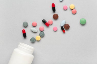 Gri arka planda farklı haplar içeren şişe, yakın plan.