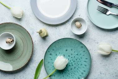 Farklı temiz tabaklar, bıldırcın yumurtaları, oyuncak tavşan ve beyaz arka planda güzel lale çiçekleri. Paskalya kutlaması