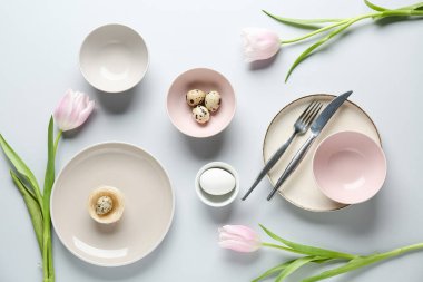 Paskalya yumurtaları ve gri arka planda güzel lale çiçekleri olan farklı temiz tabaklar.