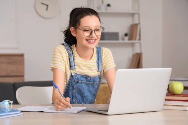 Evde dizüstü bilgisayarı ve bilgisayarı olan genç bir kız çalışıyor.