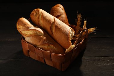 Siyah ahşap masada taze baget ve buğdaylı hasır sepet.