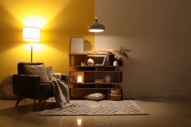 Koltuğu, kitaplığı ve parlak lambaları olan karanlık oturma odasının içinde.