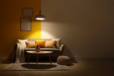 Gri kanepesi, masası ve parlayan lambası olan karanlık oturma odasının içinde.