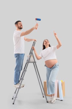Arka planda boya silindiri ve merdiveni olan hamile bir çift. Onarım kavramı