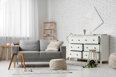 Gri kanepe, kahve masası ve deprem sonrası altüst olmuş çiçeklerle dolu dağınık bir oturma odası.