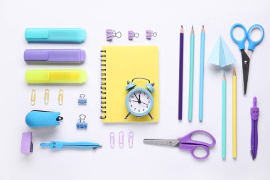 Beyaz zemin üzerinde saat, defter ve okul kırtasiyesi olan kompozisyon